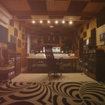 The interior of a music studio with soundproofing on the walls. The studio also has recording equipment and chairs.