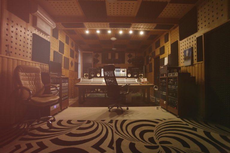 The interior of a music studio with soundproofing on the walls. The studio also has recording equipment and chairs.