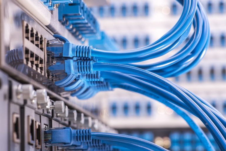 A stack of silver network boxes with dozens of light blue network cables coming out of each of them.