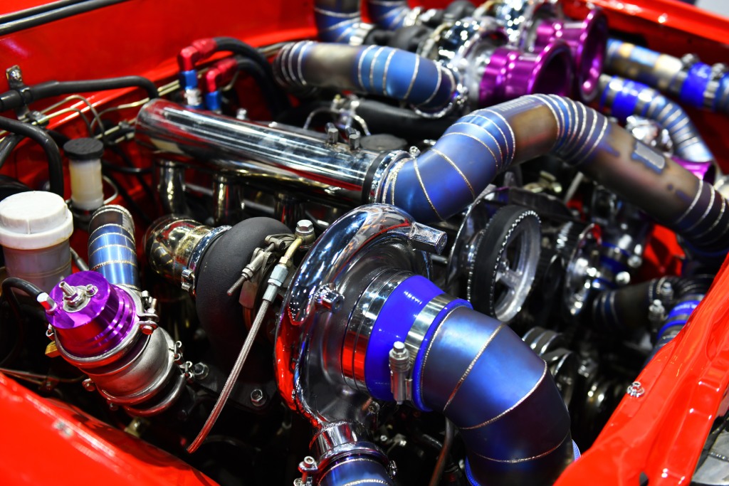A close-up view shows blue, silver, and purple vehicle engine parts on a red vehicle. Black wires are around the engine.