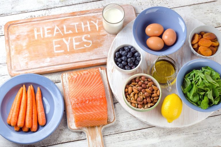 A table containing foods like eggs, salmon, vegetables, and fruits. A wooden cutting board has the words "healthy eyes" on it.