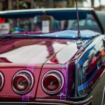 Close-up on the back of a convertible lowrider. It is painted red with pink stripes and has three round brake lights.