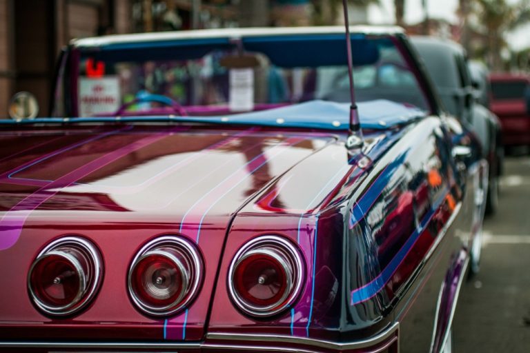 Close-up on the back of a convertible lowrider. It is painted red with pink stripes and has three round brake lights.