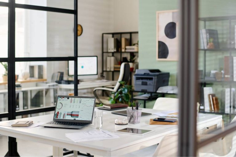 A medium sized office with two glass partition walls divides the environment from another work desk with a desktop.