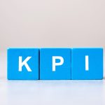 Three wooden blocks painted blue with white letters on them are lined up to spell out “KPI.”