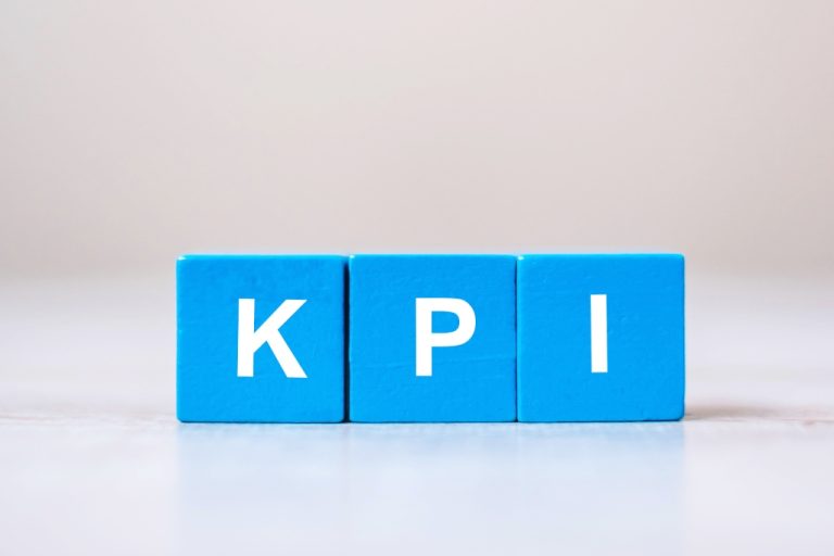 Three wooden blocks painted blue with white letters on them are lined up to spell out “KPI.”