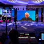 An event space with an online masterclass on multiple screens. The room is dimly lit with blue and pink lights.