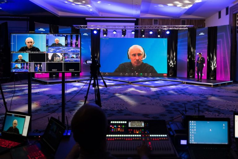 An event space with an online masterclass on multiple screens. The room is dimly lit with blue and pink lights.