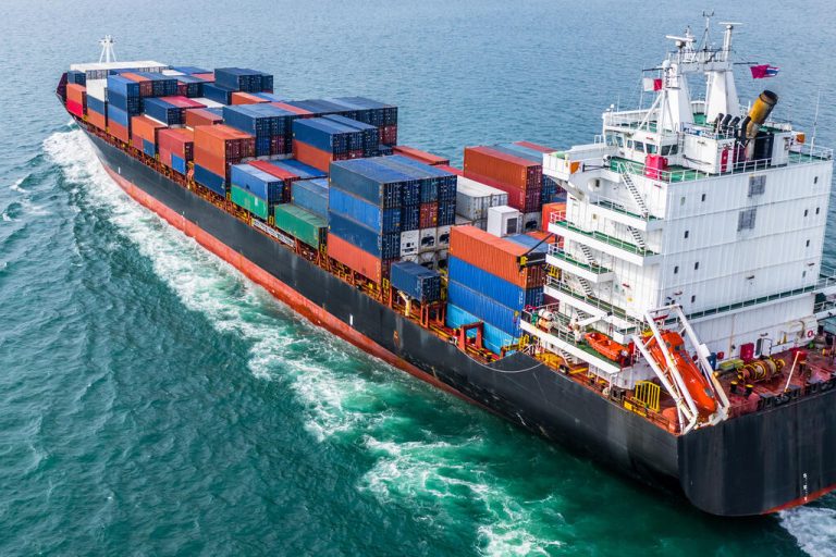 A large industrial cargo ship carrying containers of goods across the sea. The ship body is black with a white control room.