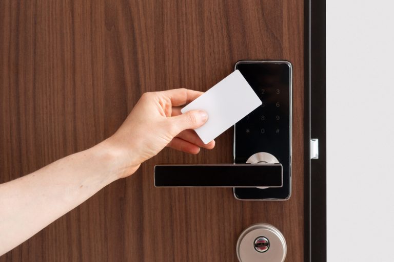 A hand placing an access control card up to the control reader. The door handle is black and the door is wooden.