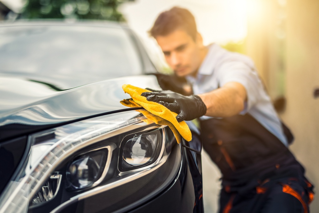 A man wearing a blue shirt and black gloves uses a yellow hand cloth to polish the exterior of a black vehicle.