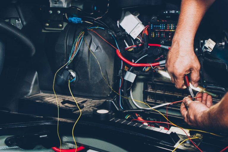 A car owner working on their vehicle's electrical system. They have wiring and parts in their hands with pliers.