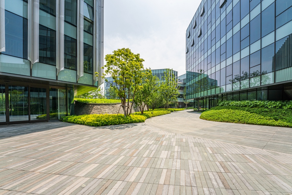 A light-colored brick walkway is between two large business buildings. Landscaping lines the walkway.