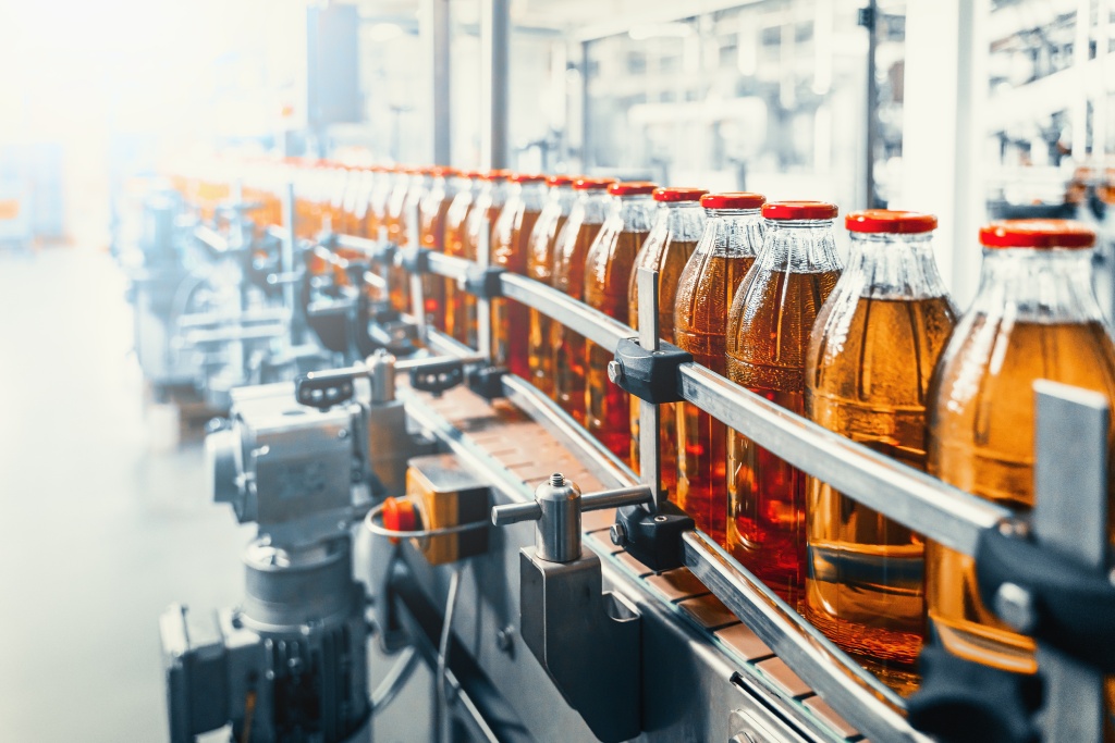 A conveyor line in a beverage production facility full of glass bottled beverages. They all have red caps.