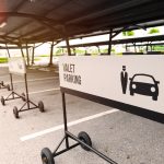 A white valet parking sign on wheels in front of an empty parking spot in a row of empty spots and valet parking signs.