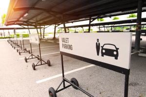 A white valet parking sign on wheels in front of an empty parking spot in a row of empty spots and valet parking signs.