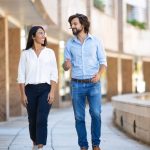 A smiling man and woman are walking in business casual clothing around an outdoor courtyard of a business building.