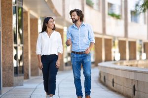 A smiling man and woman are walking in business casual clothing around an outdoor courtyard of a business building.