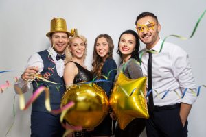 A group of event guests gathered together for a photo in a photo booth. They're smiling, wearing props like hats and glasses.