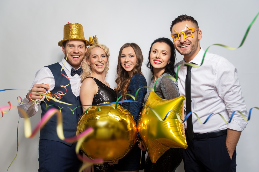 A group of event guests gathered together for a photo in a photo booth. They're smiling, wearing props like hats and glasses.