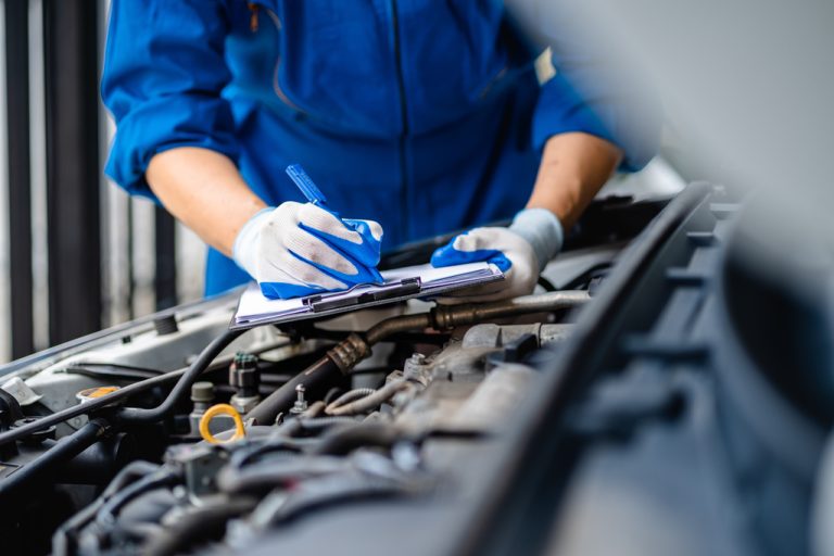 A close-up of an automotive mechanic doing maintenance and checking a list of things while wearing gloves.