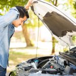 A person opening the hood of a white car and looking inside. The car is parked outside on a sunny day.