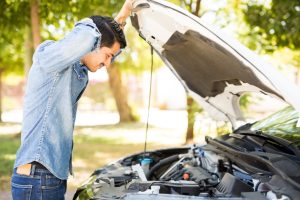 A person opening the hood of a white car and looking inside. The car is parked outside on a sunny day.