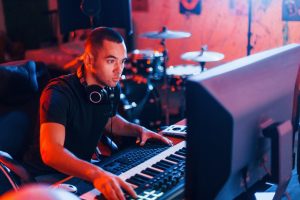 A man at an indoor studio mixing music on a large audio console with sliders, knobs, and a laptop nearby.