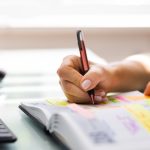 An event planner sits at their desk to create notes and plans for an upcoming event. They write in a notebook.