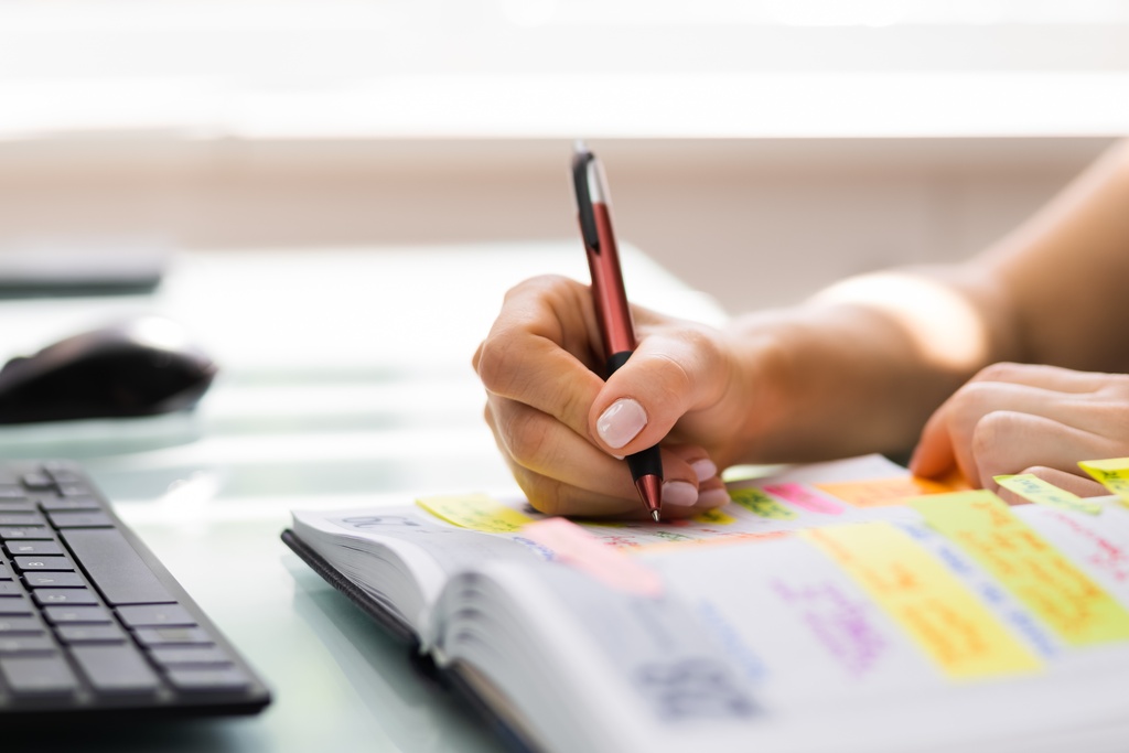 An event planner sits at their desk to create notes and plans for an upcoming event. They write in a notebook.