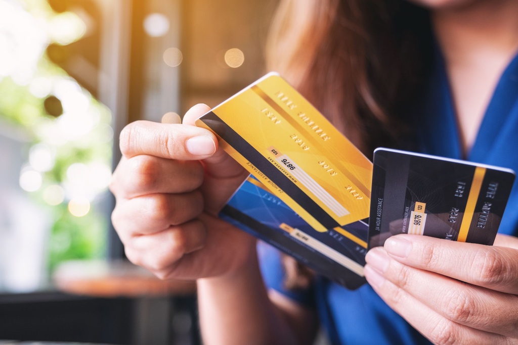 A close-up of a woman sitting down at the table holding onto three different credit cards. She wears a blue shirt.