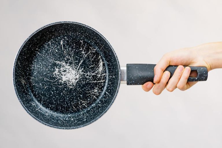 A hand holding a frying pan with a speckled ceramic coating. The pan is badly scratched in the center.