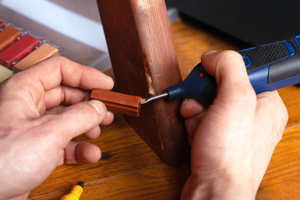 A closeup on a pair of hands using a small handheld tool to repair the leg of a chipped piece of furniture.