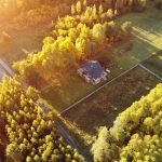 An aerial view of a small, off-grid housing unit. It is surrounded on all sides by large patches of grass and trees.