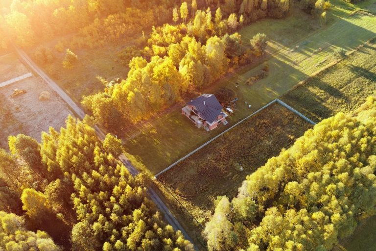 An aerial view of a small, off-grid housing unit. It is surrounded on all sides by large patches of grass and trees.