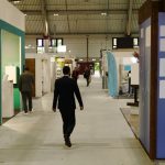 A few people walking around between brightly colored booth displays set up on a large trade show floor.