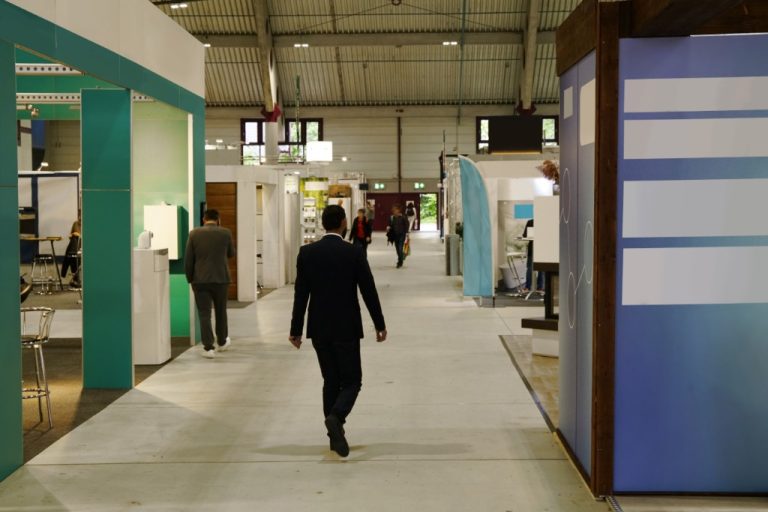 A few people walking around between brightly colored booth displays set up on a large trade show floor.