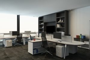A modern open office with white desks, computer monitors, black mesh chairs, and built-in shelving on a wall.