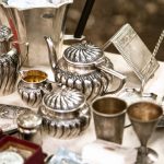 A collection of antique silver tea set pieces including a teapot, sugar bowl, creamer, goblets, and tray on a display table.