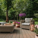 A backyard deck with multiple pieces of wicker furniture. There are also flower displays set up around the furniture.
