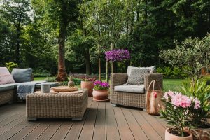 A backyard deck with multiple pieces of wicker furniture. There are also flower displays set up around the furniture.