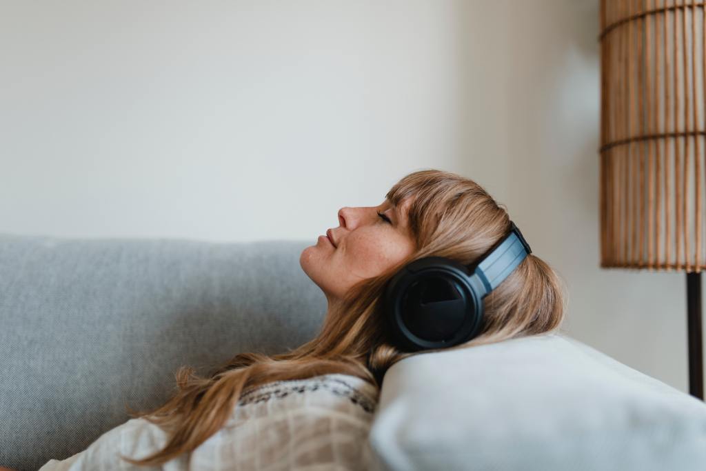 A woman closes her eyes and relaxes on a couch while wearing headphones, listening to calming music for stress relief.