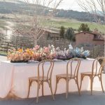 A wedding table outside next to a vineyard. The table is covered in a pink tablecloth and many colorful flowers.