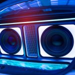 A custom car trunk audio system with two large subwoofers, LED lighting, and illuminated panels creating a vibrant blue glow.