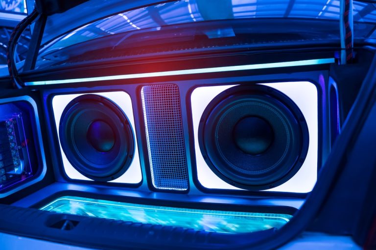 A custom car trunk audio system with two large subwoofers, LED lighting, and illuminated panels creating a vibrant blue glow.