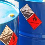 Two blue hazardous containment barrels. They have stickers on the side of them that say they are corrosive and flammable.