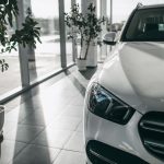 A close-up of the front headlight and grille of a white modern car in a display area of a dealership.