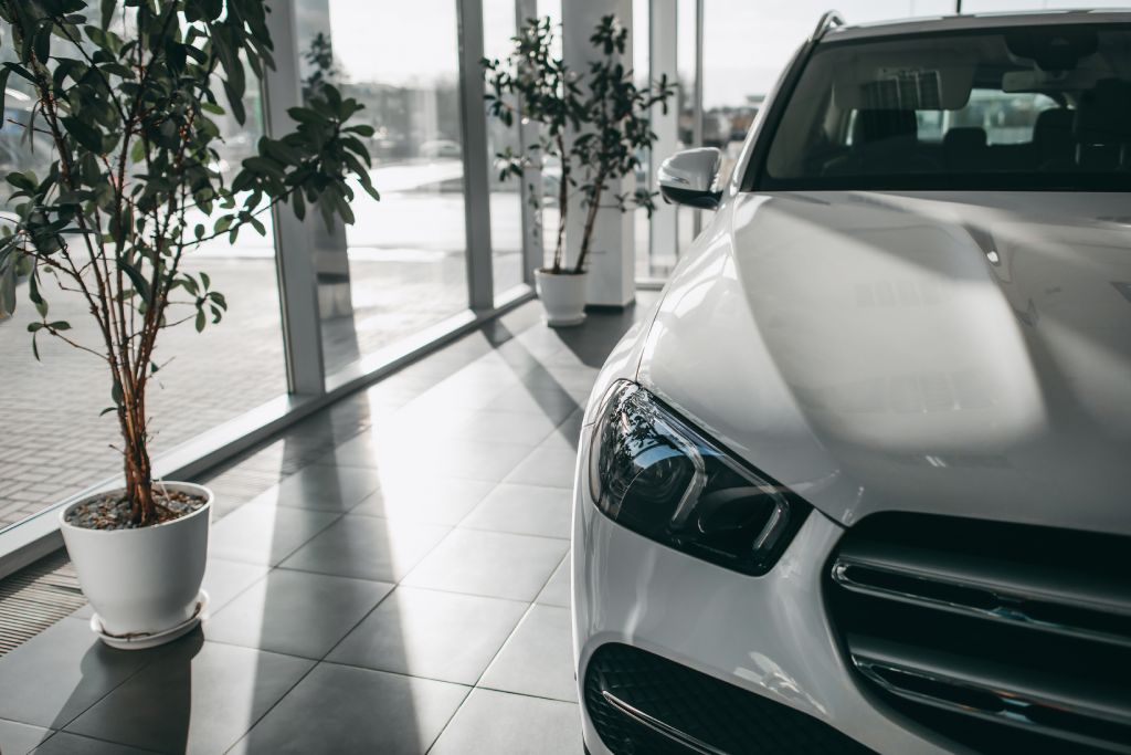 A close-up of the front headlight and grille of a white modern car in a display area of a dealership.
