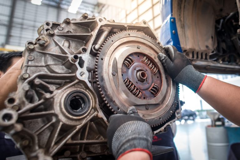 A close-up of a pair of hands with gloves grabbing the flywheel from a removed engine block of a car in a repair shop.