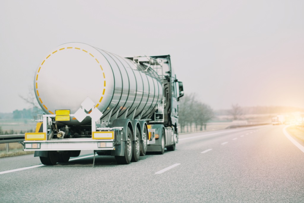 A truck is driving down a road away from the camera. There are no other cars on the road.